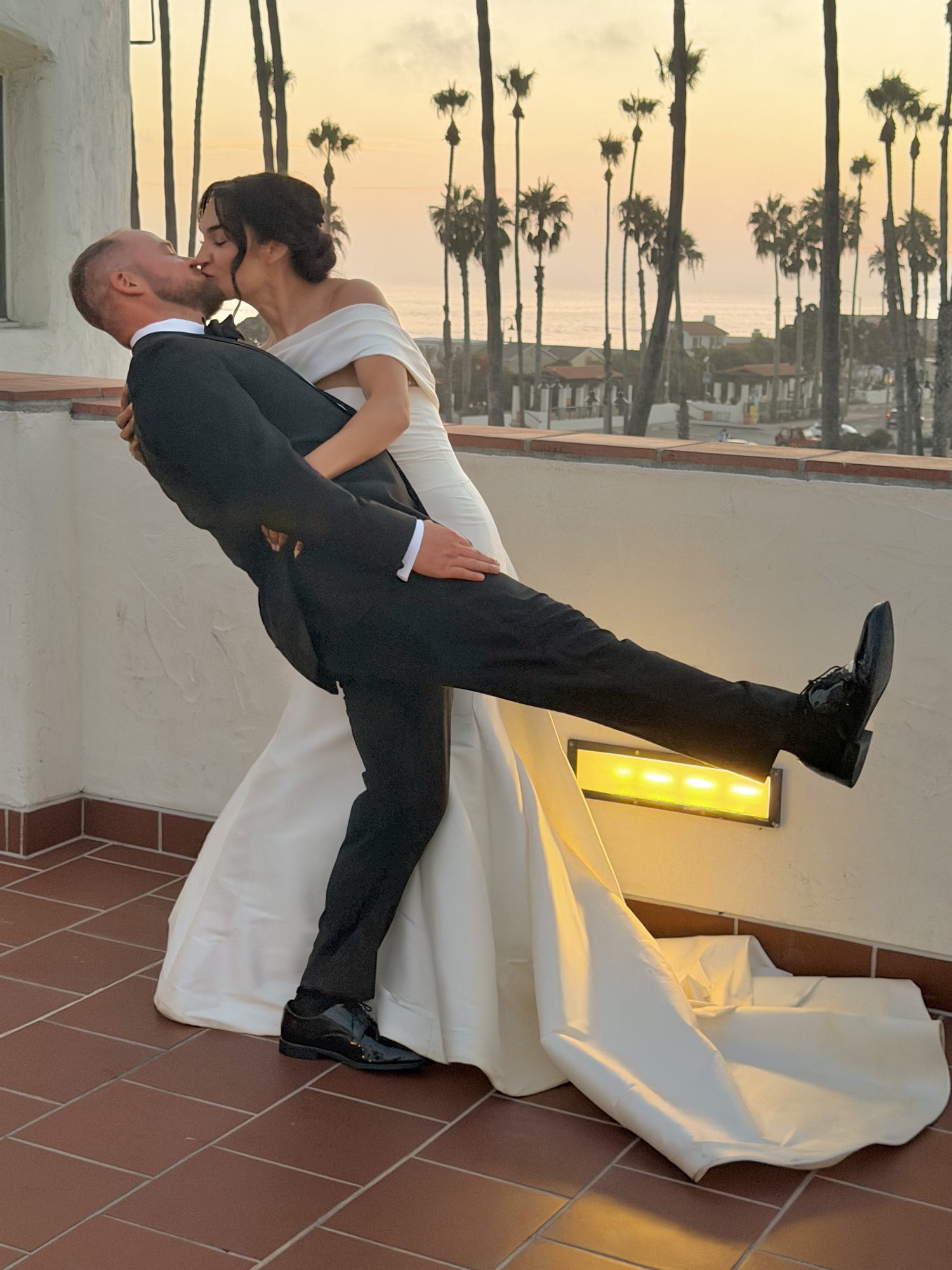 Bride and groom dip kiss at sunset on rooftop balcony