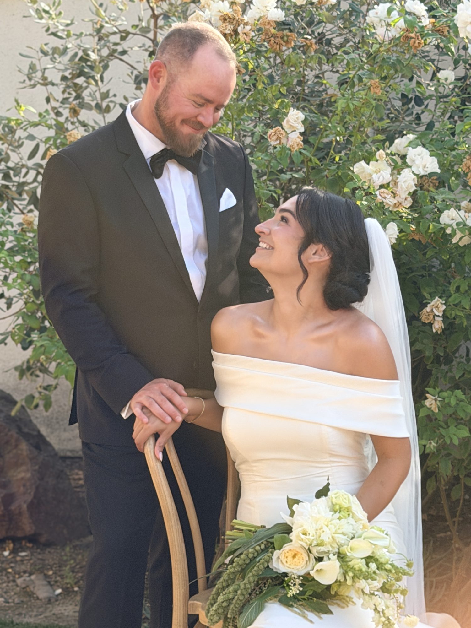 Bride and groom smiling close together by a rose bush