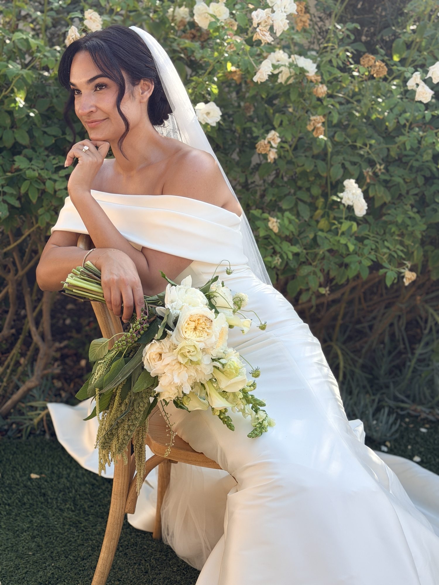 Bride seated in chair with bouquet and veil, smiling