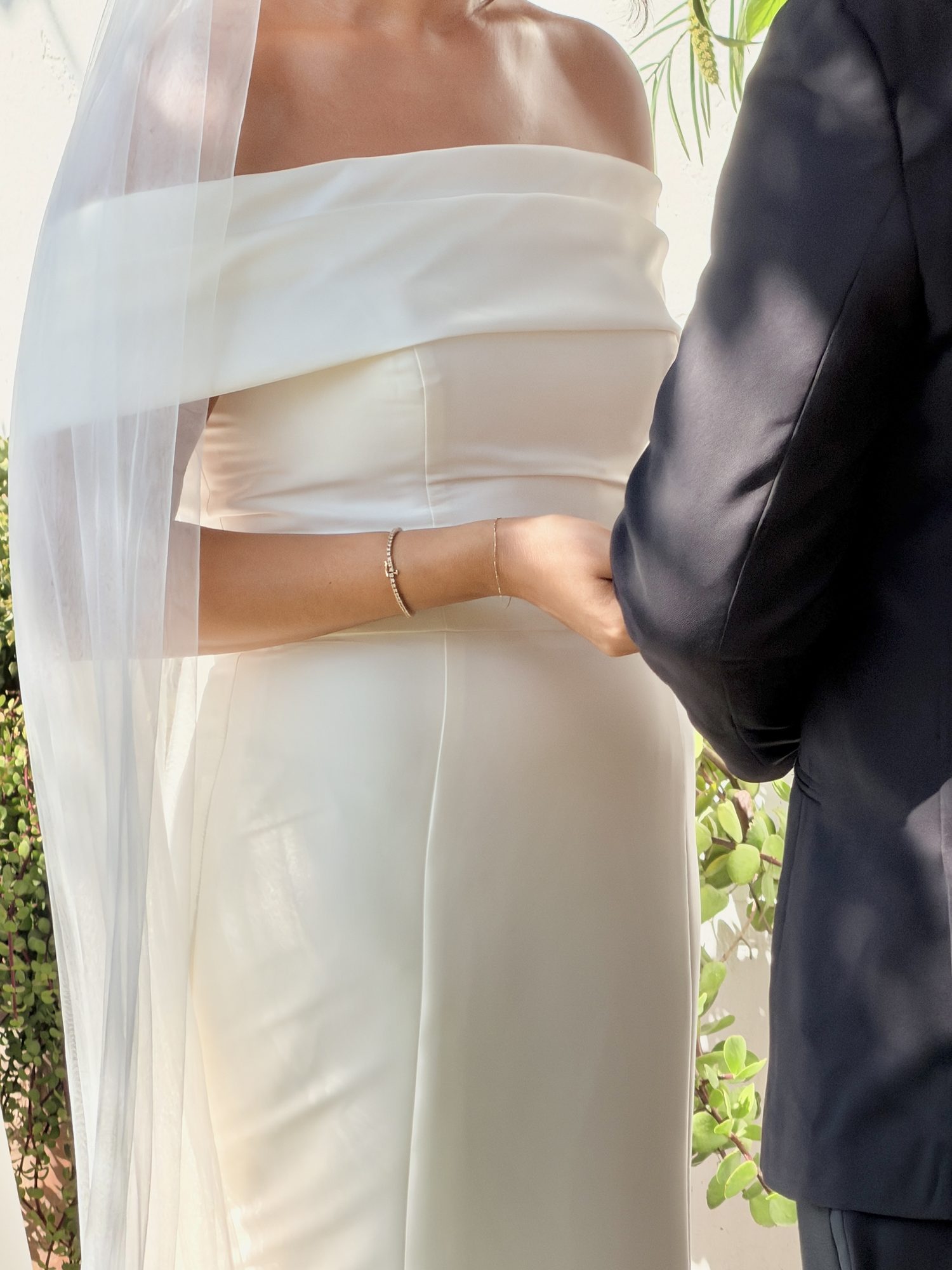 Bride and groom holding hands, veil and bracelet detail