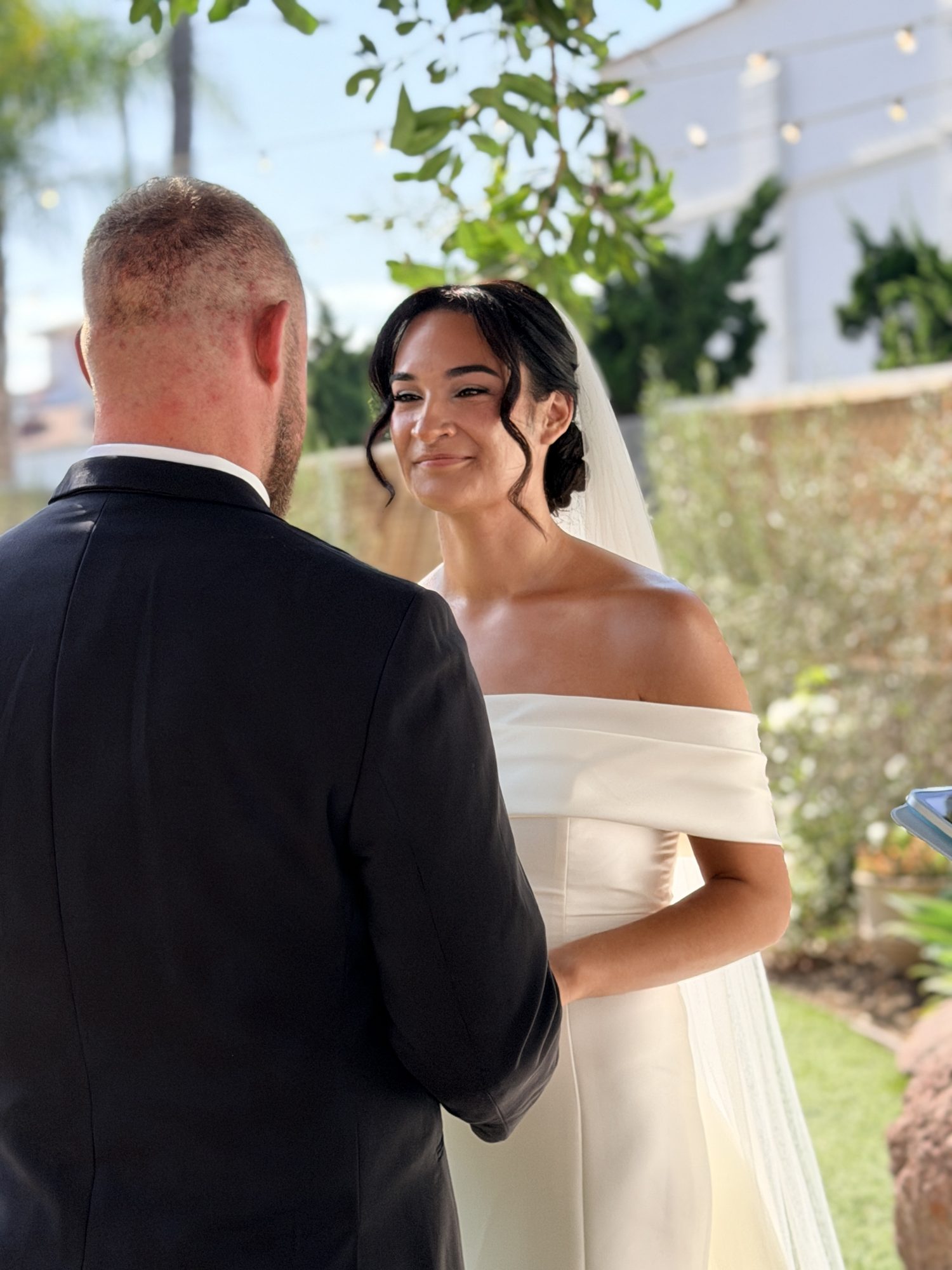 Bride and groom smiling, backs to camera at outdoor ceremony