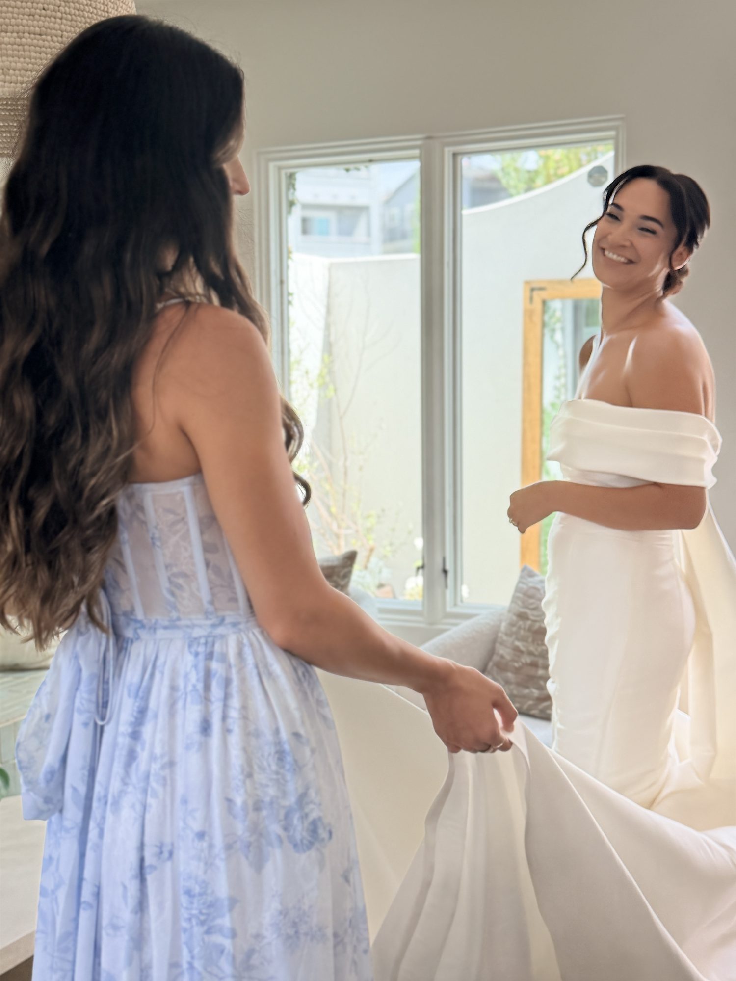 Bride getting dressed as bridesmaid holds the train