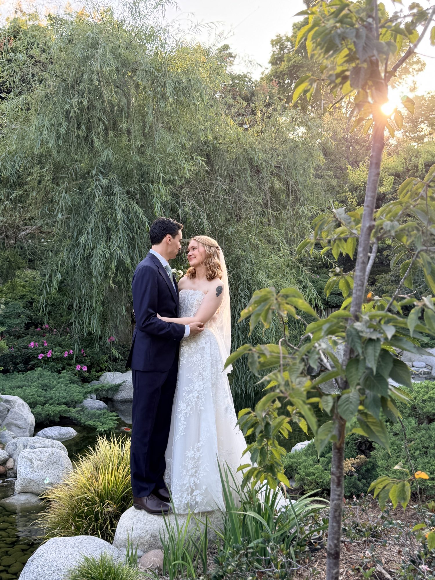Bride and groom embracing under willow trees at sunset